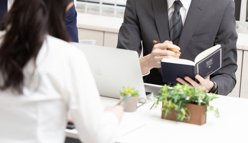 会議の内容を手帳に書き込むスーツ姿の担当者