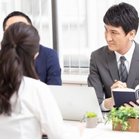 オフィスで会議をする男性がデスクで資料を確認の写真