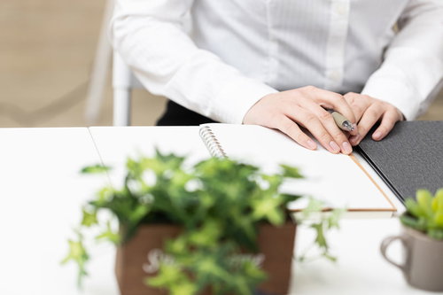 テーブルの上にノートを出して書く女性の手元