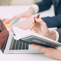 ノートパソコンと手帳にスケジュールを書き込むの写真