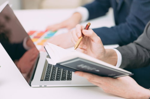 ノートパソコンと手帳にスケジュールを書き込む