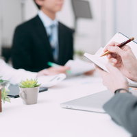 会議中の内容を手帳にペンでメモする手元と資料の写真