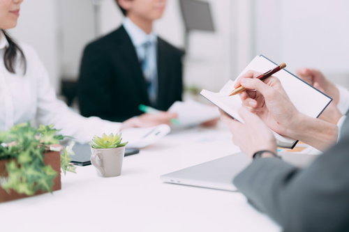 会議中の内容を手帳にペンでメモする手元と資料