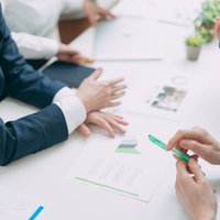 テーブル上に資料を広げてスーツ姿で会議をする様子の写真