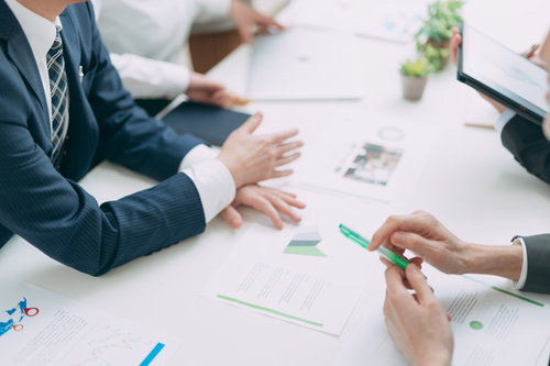 テーブル上に資料を広げてスーツ姿で会議をする様子