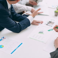 執拗に提案を繰り返す営業マンと会議中の資料検討の写真