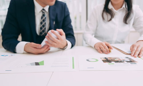 資料を見ながら検討する上司と部下の女性との打ち合わせ