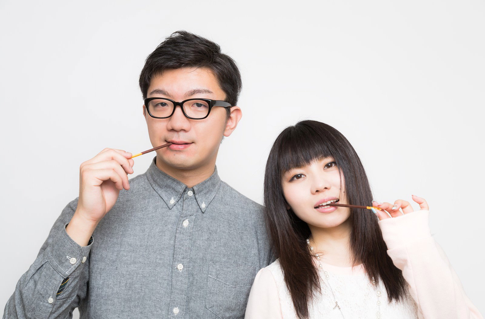 灰色シャツの眼鏡男性と白トップスの黒髪女性がポッキーをくわえて向き合う［モデル：OZPA lala］