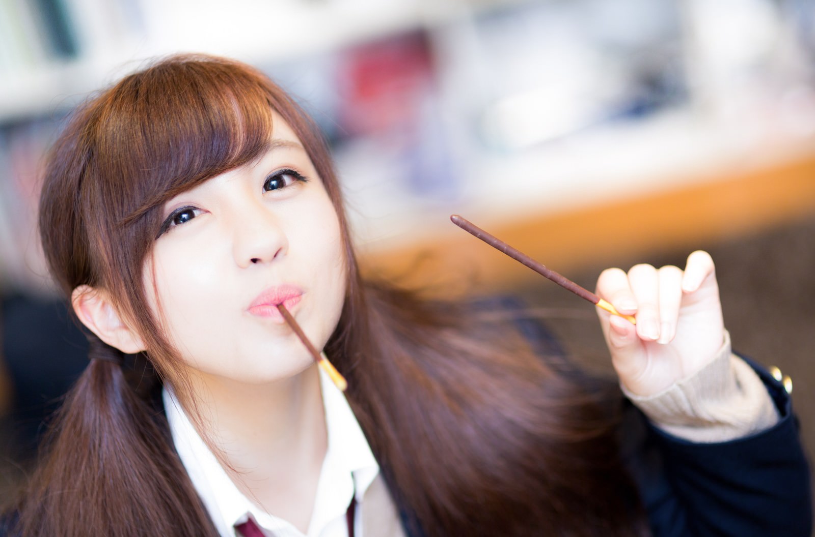 ポッキーを持って上を見ながら微笑む制服姿の女子高生［モデル：河村友歌］