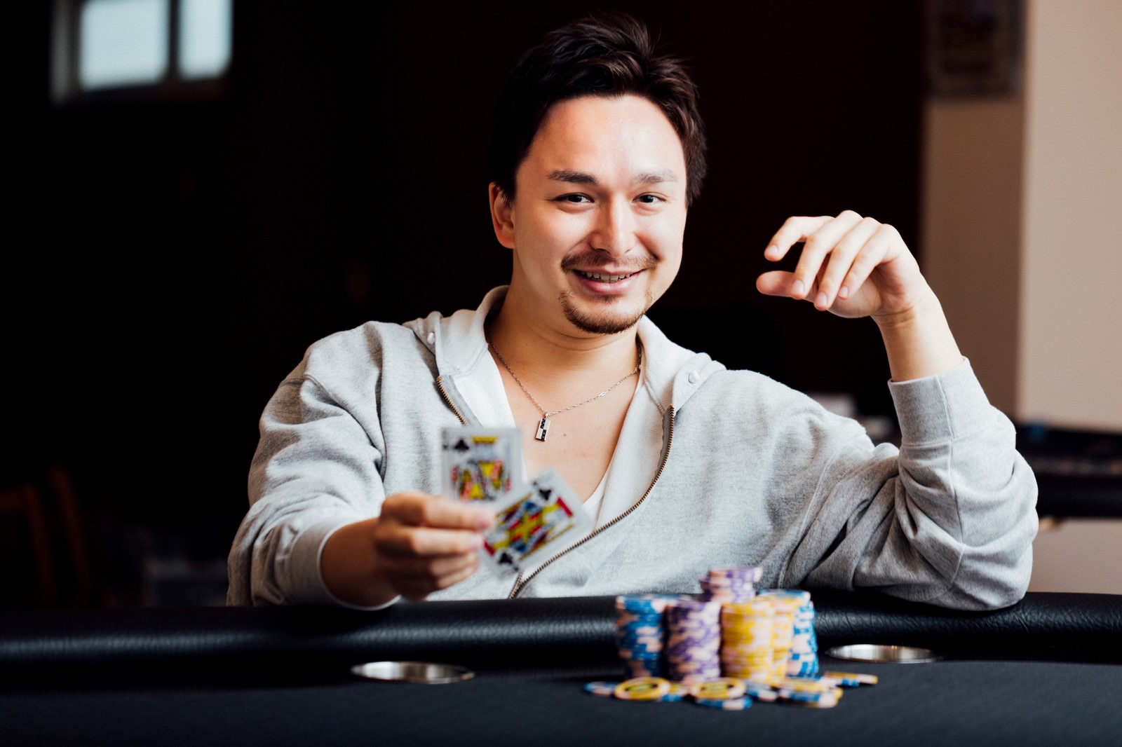 ポーカーテーブルでカードを持ち表情をひきつらせる男性プレイヤー［モデル：Max_Ezaki］