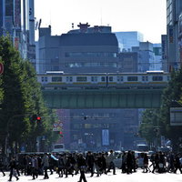 横断歩道を渡る人混みと高架の電車の写真