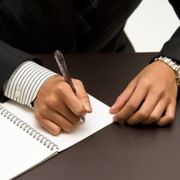 ノートにペンで書きこむビジネスマンの手元の写真