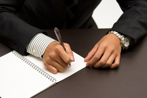 ノートにペンで書きこむビジネスマンの手元