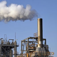 青空に白い煙をふく工場の煙突の写真