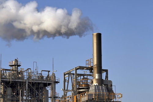 青空に白い煙をふく工場の煙突