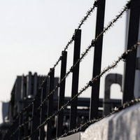 曇り空を背景に張られた工場の有刺鉄線の写真