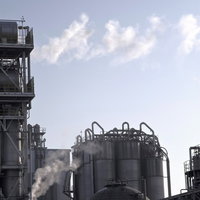 曇り空の下に立つ工場の配管とタンクの写真