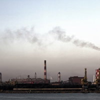 曇り空の下で煙をあげる対岸の工場の写真