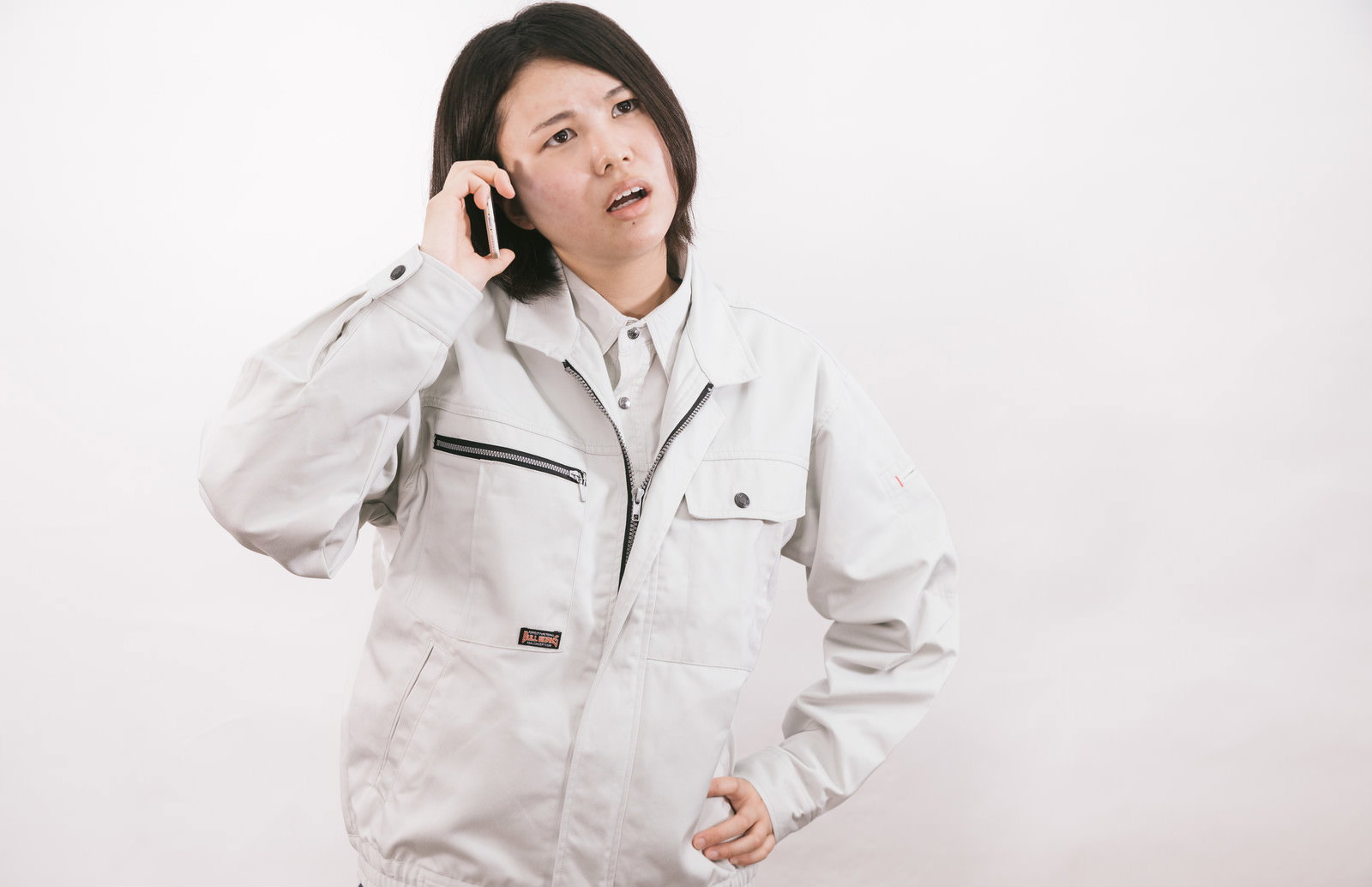 白い作業着を着た女性がスマートフォンで通話しながら困った表情を見せている［モデル：佐竹PP］