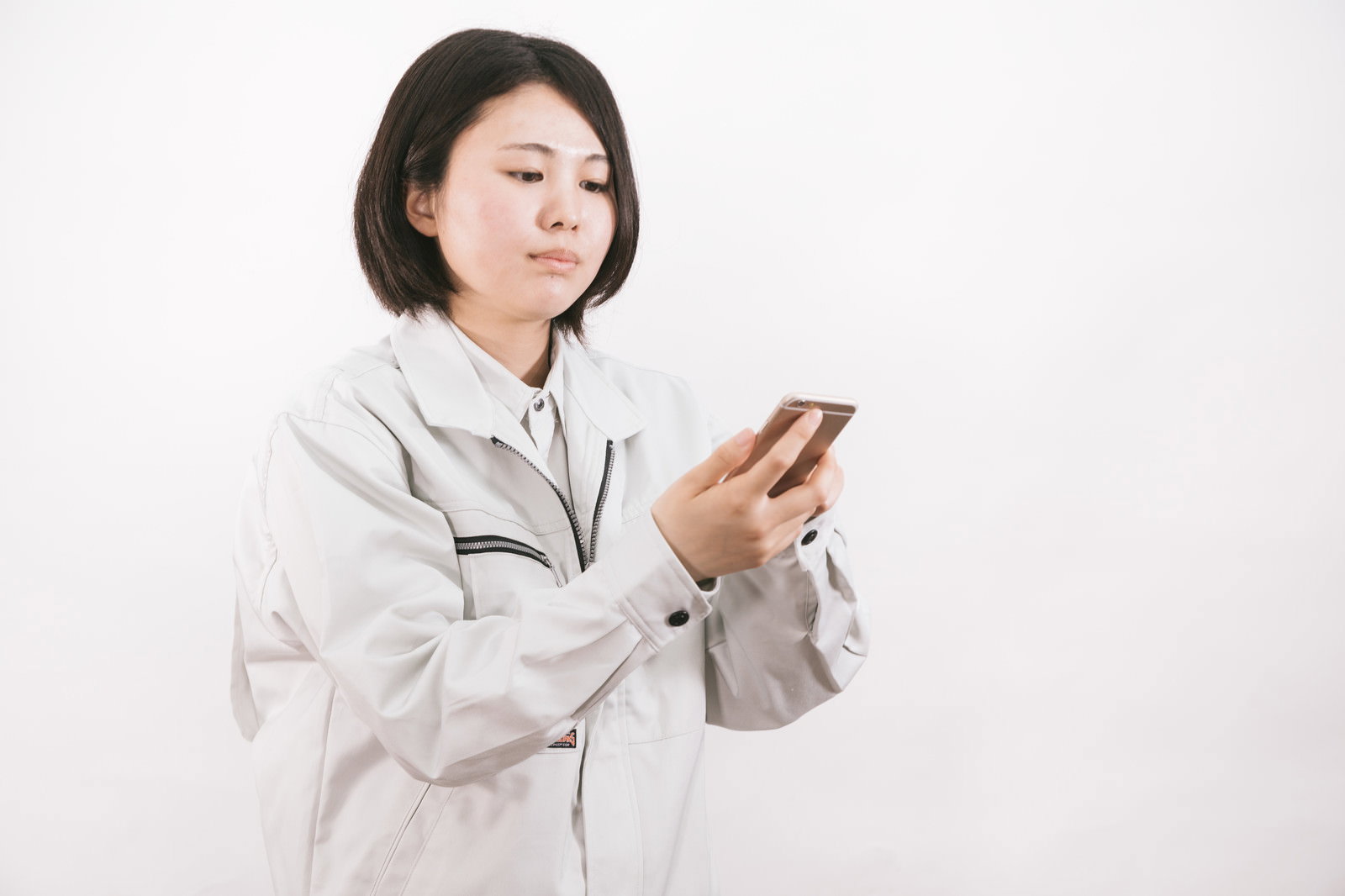 グレーの作業着を着た女性がスマートフォンを操作している［モデル：佐竹PP］