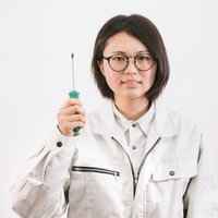 ドライバーを持った作業着姿の眼鏡をかけた女性の写真