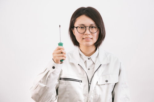 ドライバーを持った作業着姿の眼鏡をかけた女性