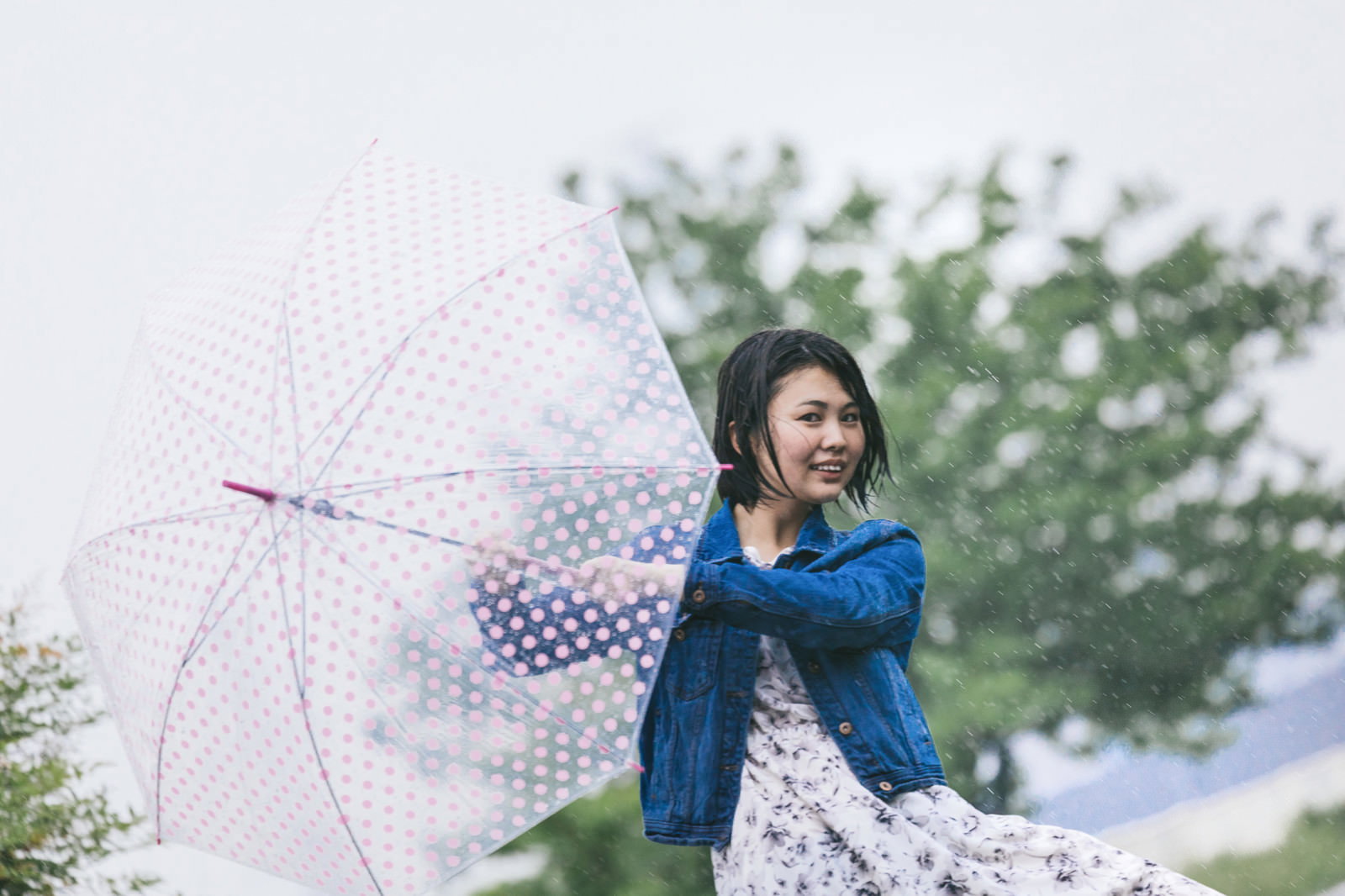 雨の中で水玉模様の傘を持ち楽しそうな表情の青いトップスを着た女性［モデル：佐竹PP］