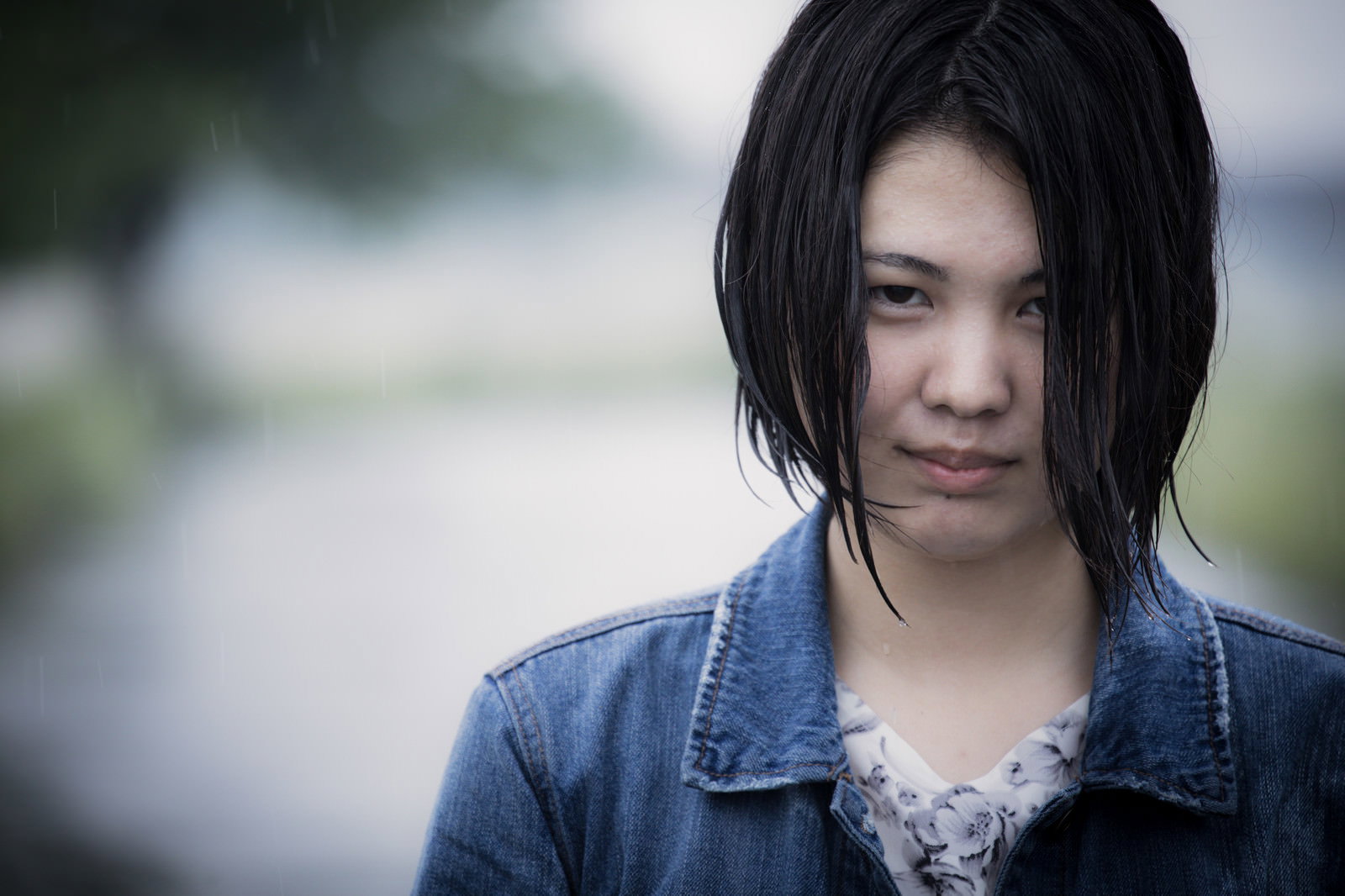 雨に濡れたデニムジャケット姿の女性が薄ら笑いを浮かべている様子［モデル：佐竹PP］