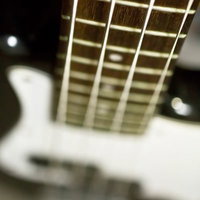 フレットとポジションマークが見えるベースのネックと弦の写真