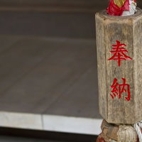 赤い「奉納」の文字が書かれた古い柱と鈴緒の写真