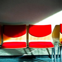 室内に並ぶ赤い座面と金属脚の無機質なベンチの写真