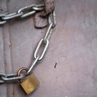 塗装が剥がれた古いドアに掛かる南京錠と鎖の写真