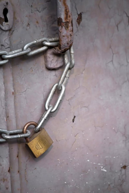 塗装が剥がれた古いドアに掛かる南京錠と鎖
