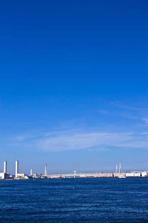 青い海の向こうに見える横浜の港湾施設と煙突