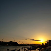 夕焼けのグラデーションに染まる漁港のボートとクレーンの写真