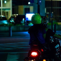 緑のヘルメットで走り去る二人乗りバイクの後ろ姿の写真