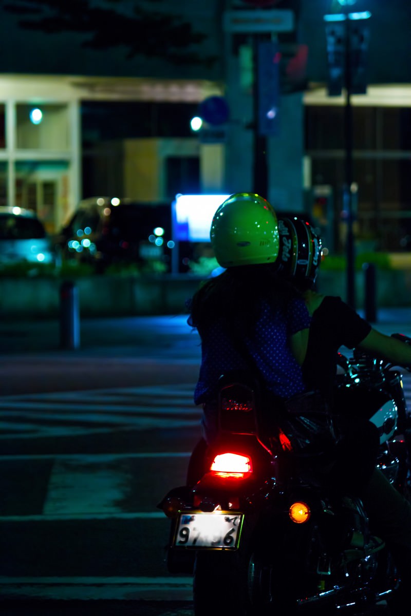 緑のヘルメットで走り去る二人乗りバイクの後ろ姿