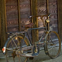 木の板壁の前に立てかけた革サドルの古びた自転車の写真