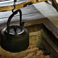 古い梁の下に鎖で吊るされた囲炉裏の黒い鉄瓶の写真