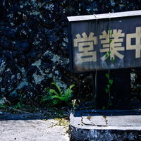 ツタや草に覆われた灰色の壁の朽ちた営業中の看板の写真