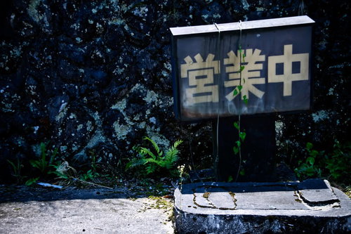 ツタや草に覆われた灰色の壁の朽ちた営業中の看板