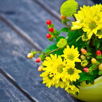 青灰色の板の上に置いた黄色い花の丸い花瓶の写真