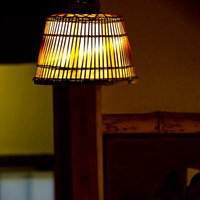 暗い室内で温かく光る竹編みの傘型ランプシェードの写真
