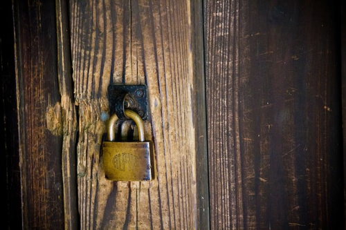 風化した木の板壁に掛かる金色の南京錠と黒い金具