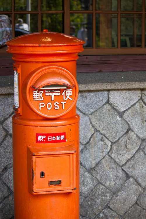 石の壁の前に立つオレンジ色の昔の丸型郵便ポスト