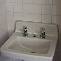 白いタイル壁に付いた2つの蛇口がある無機質な洗面台の写真