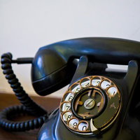 木のテーブルに置いたダイヤル式のレトロな黒電話の写真