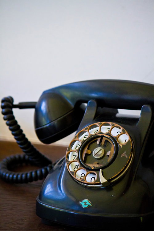 木のテーブルに置いたダイヤル式のレトロな黒電話