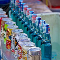 金属の台に並ぶ露店のラムネとお酒の瓶と缶の写真