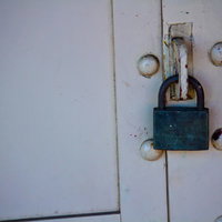 白い扉に掛かった緑色の錆びた南京錠と金具の写真